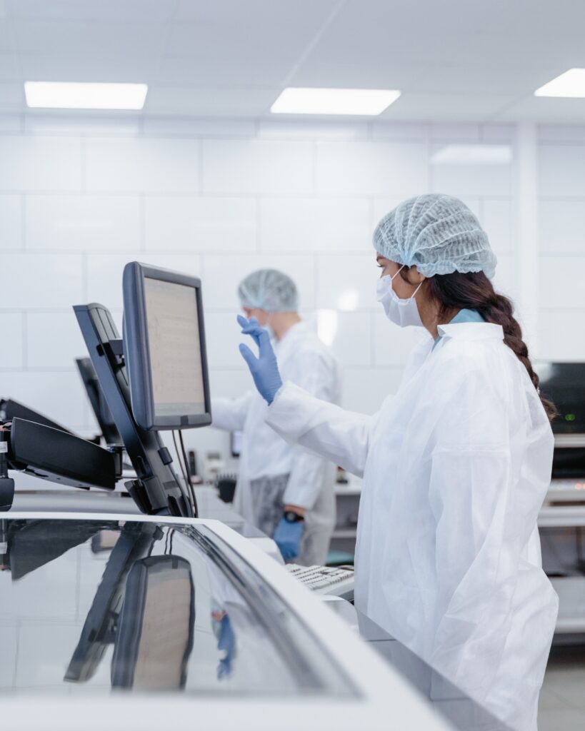 Laboratory personnel in cleanroom attire interacting with computers.
